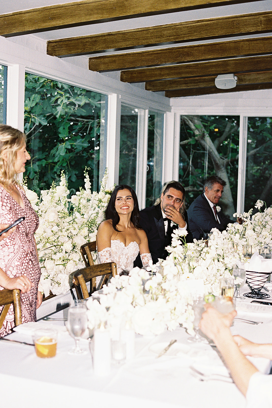 A couple sits at a table holding up wine glasses. The table is decorated with white flowers and candles.