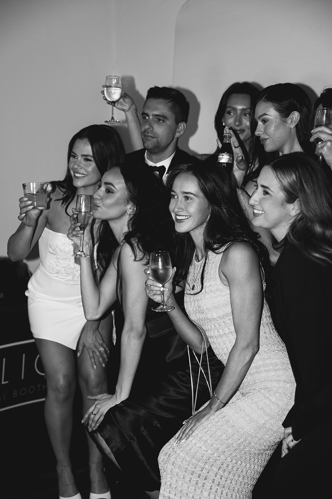 A group of people posing together at a party, holding drinks and smiling, in a black and white photograph.