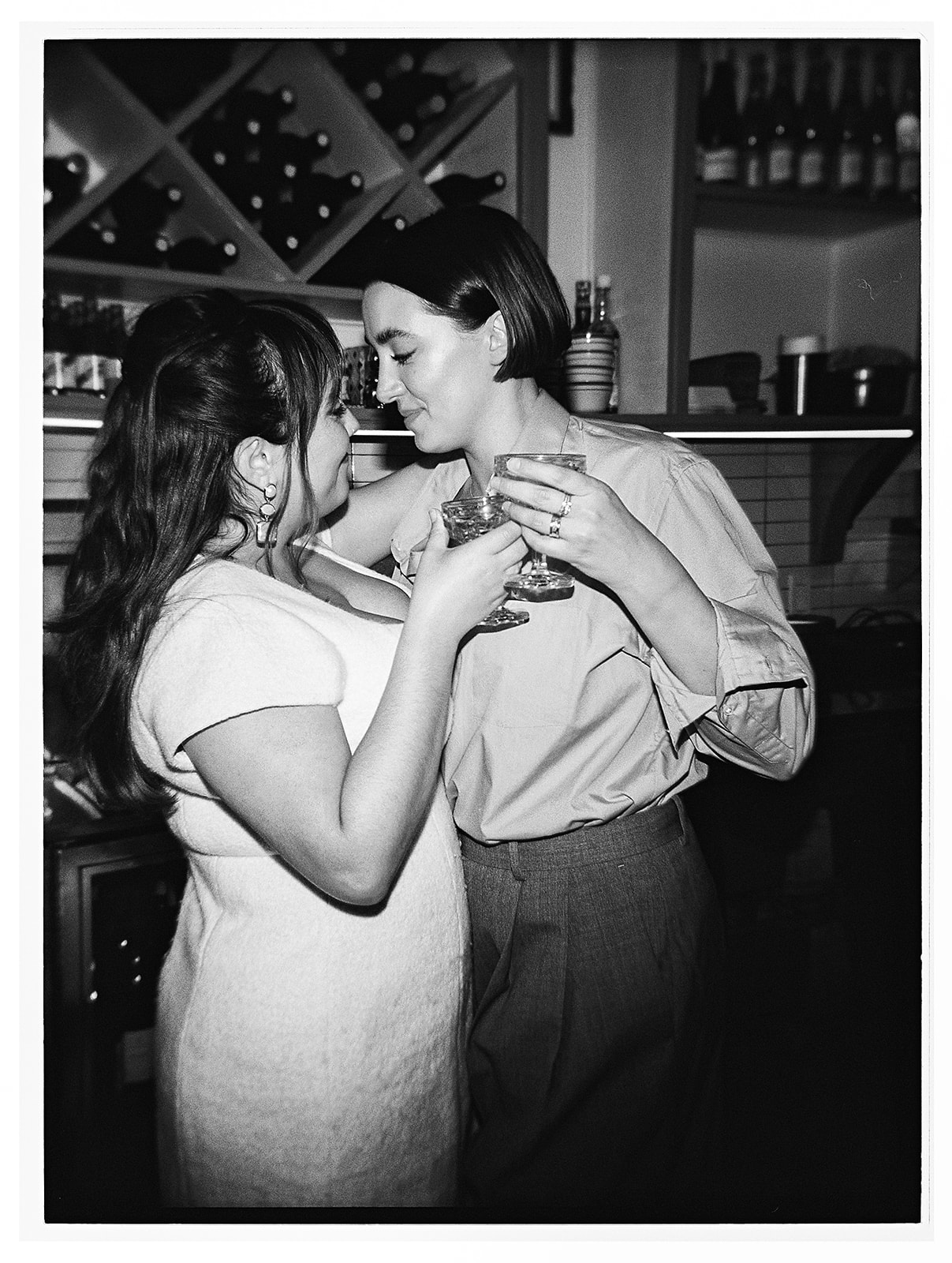 Two people clink glasses in a toast at a table, with a bouquet of white flowers and a dish in the background.